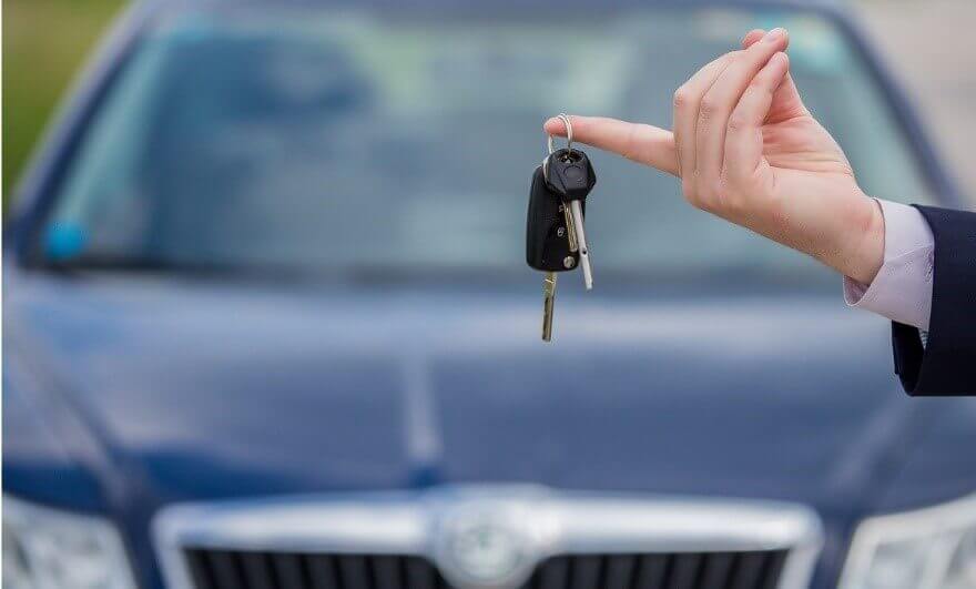 A car dealer holding car keys in front of a used car for sale