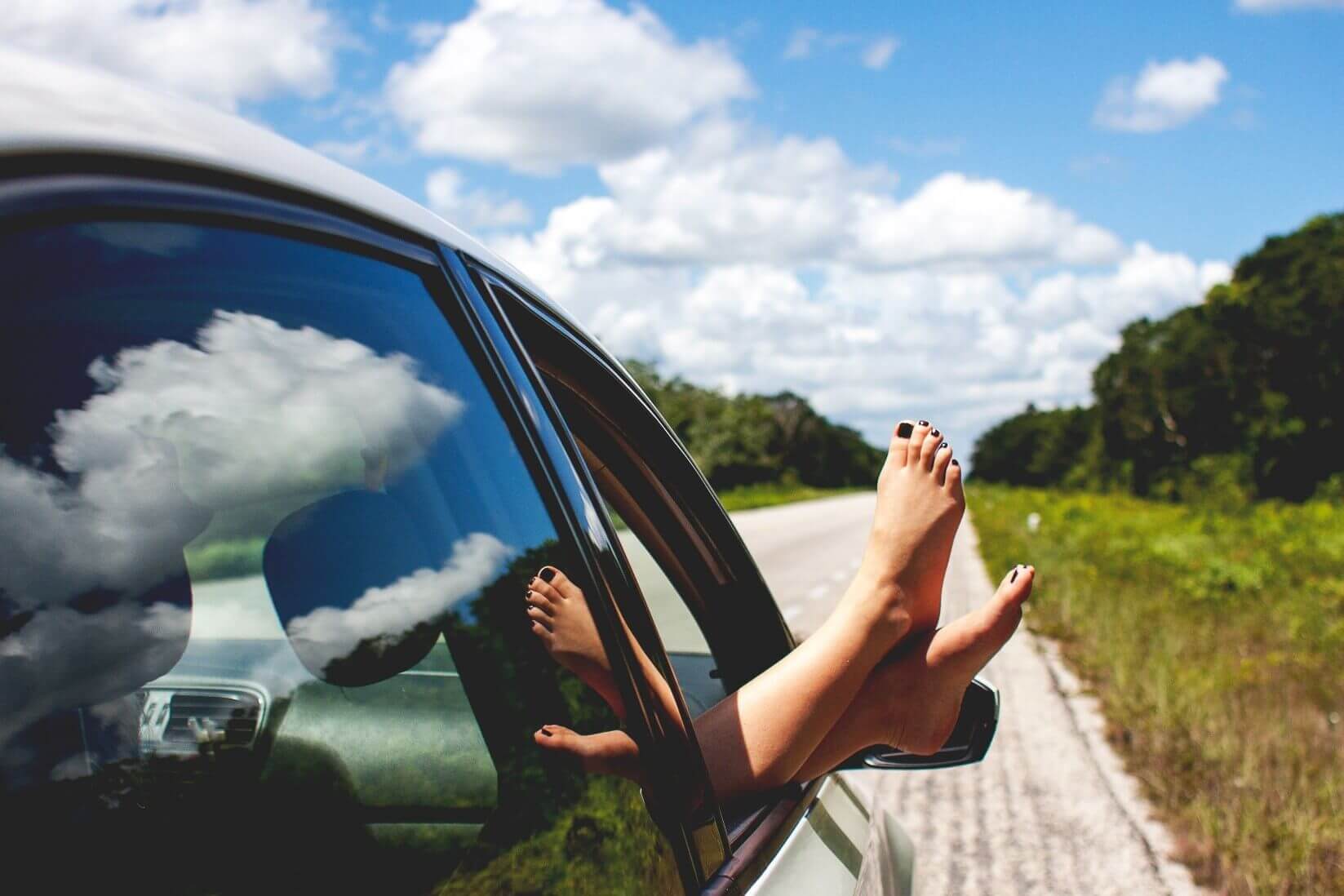 Woman puts her feet out of the car on a sunny day