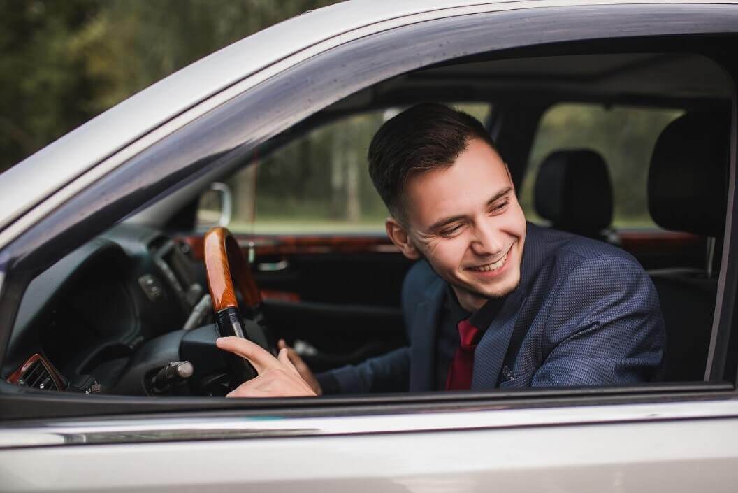 business man in a dark suit smiling while driving a car